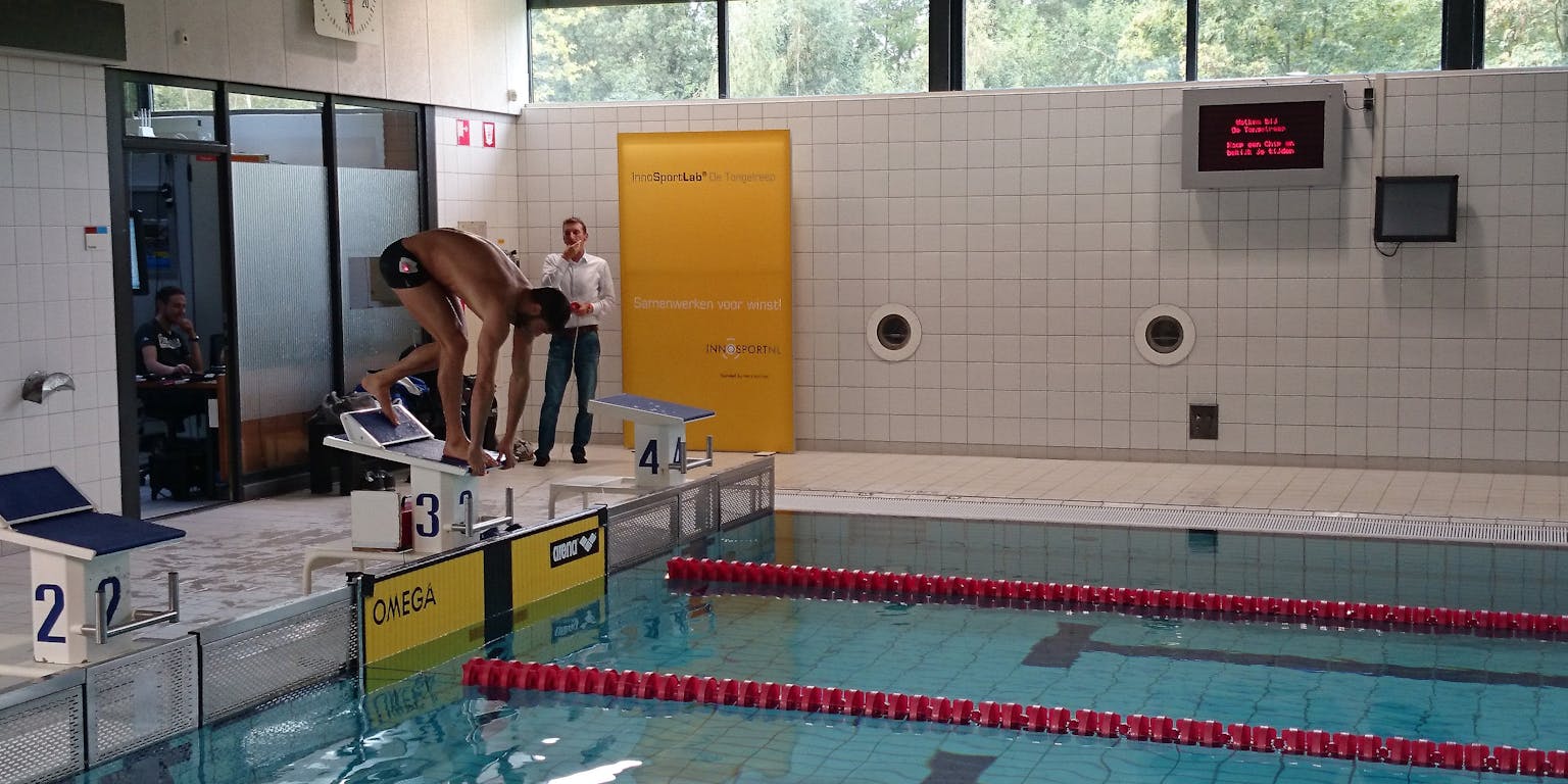 Een zwembad om banen te trekken. Er staat een persoon in de startblokken om in het water te springen.