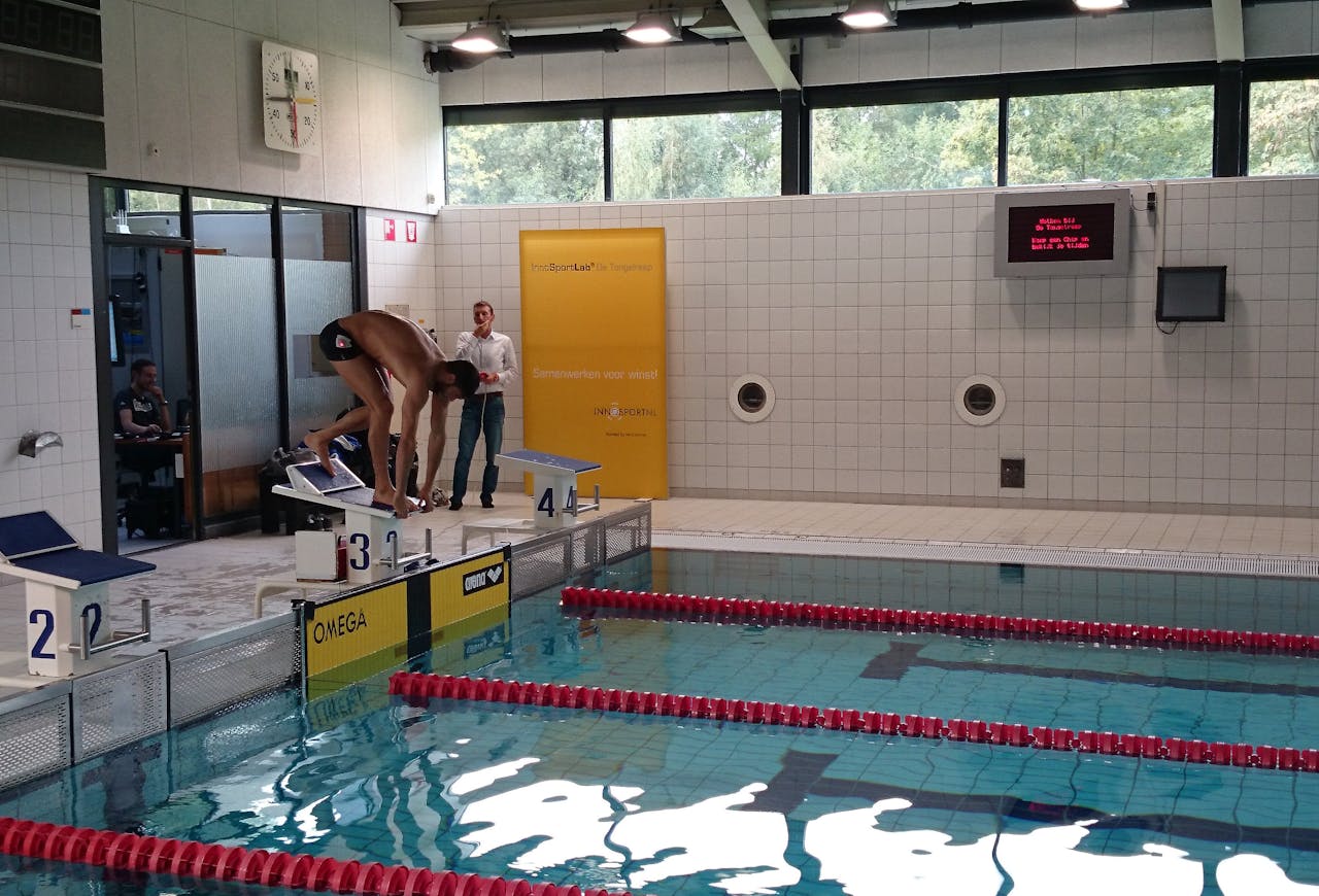 Een zwembad om banen te trekken. Er staat een persoon in de startblokken om in het water te springen.