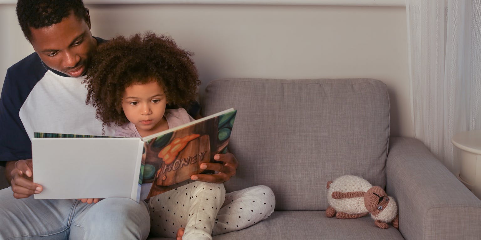 Een man en een meisje lezen een boek op een bank.