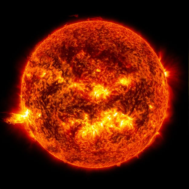 Uitbarsting op de zon (links) die geladen deeltjes, zoals protonen en elektronen, met hoge snelheid de ruimte in stoot. Zo’n plasmawolk kan de aarde in een tot drie dagen bereiken. Op een zwarte achtergrond is een grote bol te zien, de zon. Het oppervlak is oranje en zwart met felle gele lichtgevende plekken.