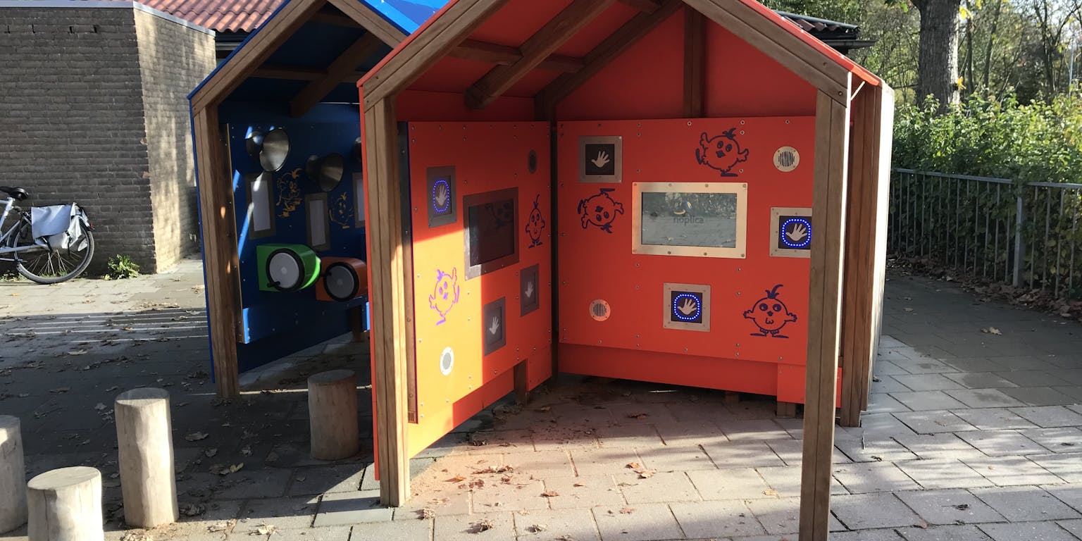 Twee houten speelhuisjes in een park met een blauwe en oranje dak.