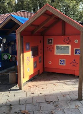 Twee houten speelhuisjes in een park met een blauwe en oranje dak.