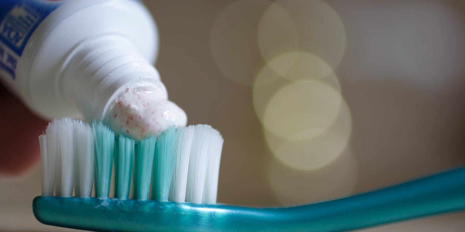 Een close-up van een blauwe tandenborstel waar tandpasta op wordt gedaan.