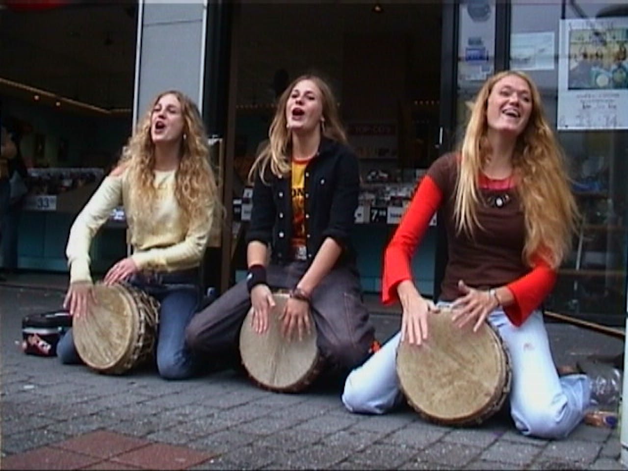 Drie vrouwen zitten op de stoep met trommels.