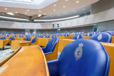 Tijdens vergaderingen van de commissie Digitale Zaken komen doorgaans maar weinig leden opdagen. Een grijze vergaderzaal met houtkleurige banken en stoelen met blauwe bekleding.