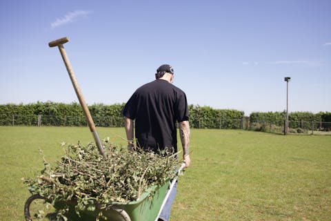 Een taakstraf wordt door velen gezien als ‘soft’, maar de kans op herhaling is kleiner dan na een gevangenisstraf Man op de rug gezien die een volle kruiwagen met groenafval achter zich aan trekt