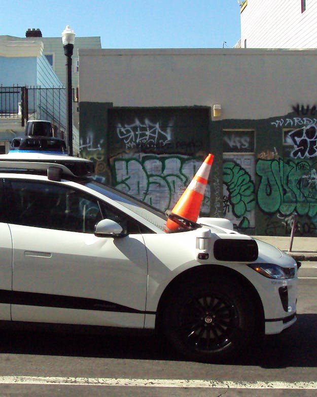 In San Francisco werden zelfrijdende auto’s in 2023 geplaagd door actievoerders die met verkeerspionnen camera’s en sensoren van de auto bedekten, waardoor de auto’s niet konden wegrijden. Zijaanzicht van een Waymo taxi in San Francisco, met een verkeerspion op de voorruit om de sensor te bedekken.