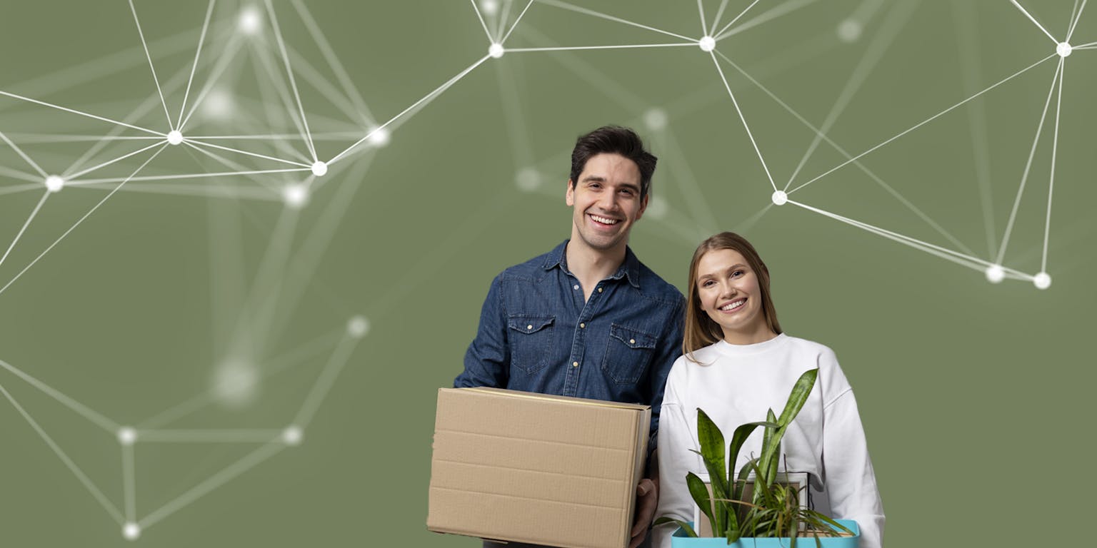 Een jongeman met donker haar en een jongedame met blond haar lachen naar de camera. De jongeman houdt een kartonnen doos vast, de jongedame een plant in een plantenbak.