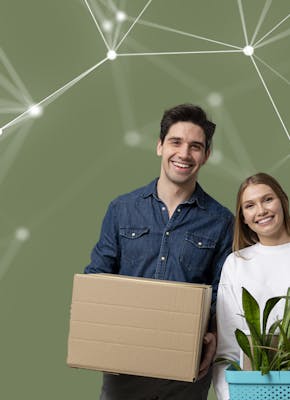 Een jongeman met donker haar en een jongedame met blond haar lachen naar de camera. De jongeman houdt een kartonnen doos vast, de jongedame een plant in een plantenbak.