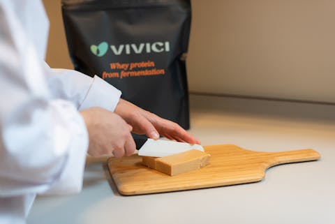 Wei-eiwit is het deel van zuivel dat je niet gebruikt bij het maken van kaas. Het is vooral bekend bij krachtsporters als eiwitaanvulling. De koe is binnenkort niet meer nodig, als het aan onderzoekers ligt. Iemand in een labjas snijdt een deel af van een geel blok wei-eiwit