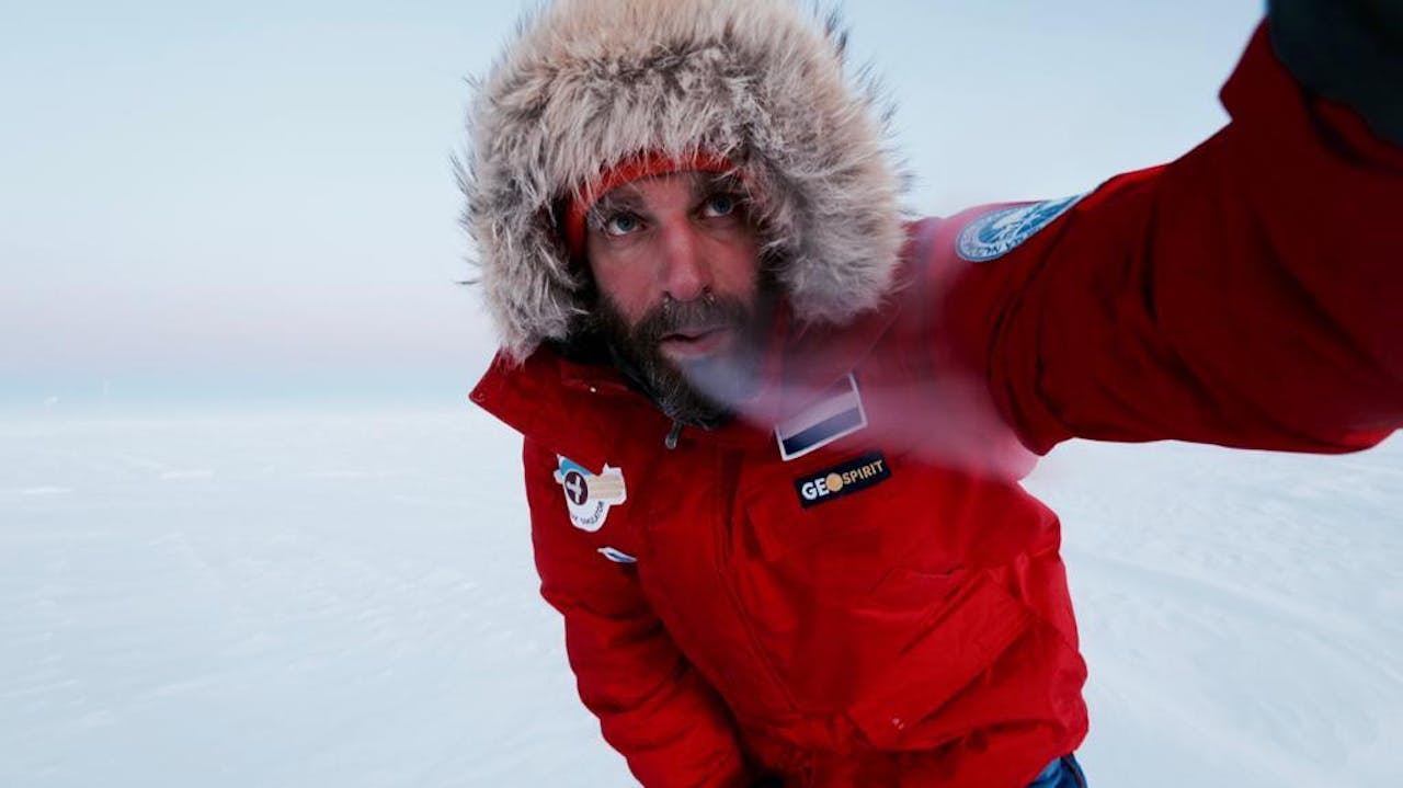 Een man in een rode jas maakt een selfie in de sneeuw