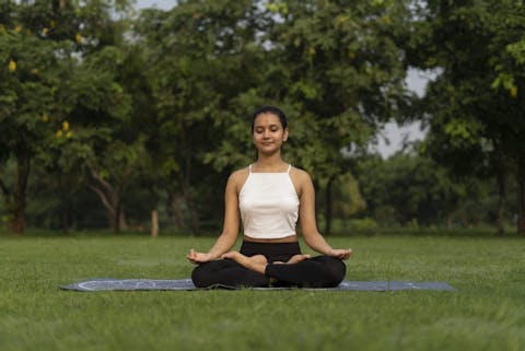 Even weg vanachter je bureau of computerscherm en naar buiten toe, is een goede manier om overprikkeling tegen te gaan. Vrouw doet aan yoga in het park