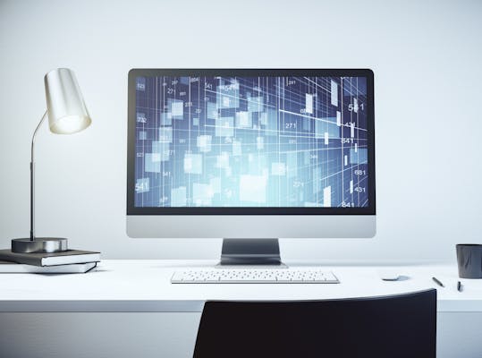 Stilleven van een computerscherm op een wit bureau met zilverkleurige bureaulamp, wit toetsenbord, zwarte mok en zwarte pennen. Op het scherm is een abstract grafisch patroon te zien.