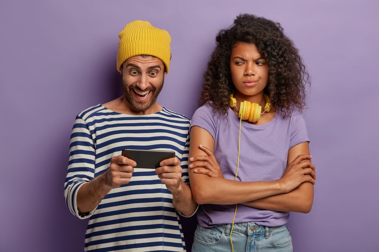 jonge man kijkt blij naar telefoon, vrouw kijkt geirriteerd