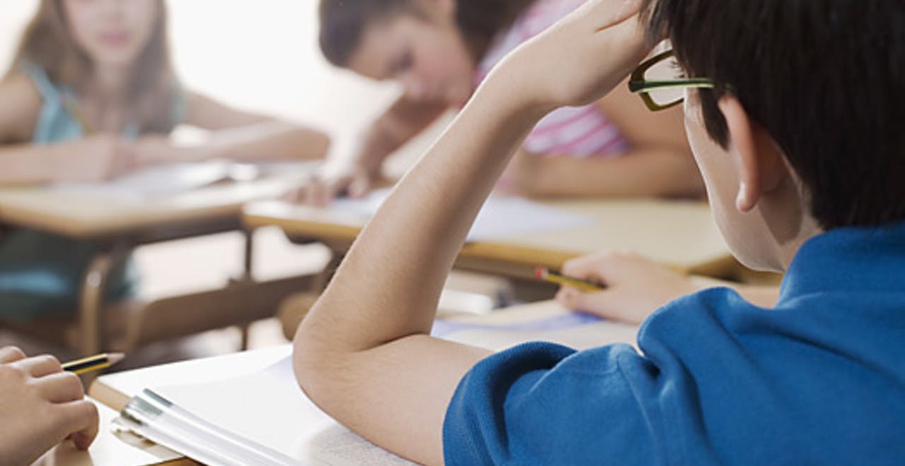 In een klaslokaal zit een jongen aan een bureau.