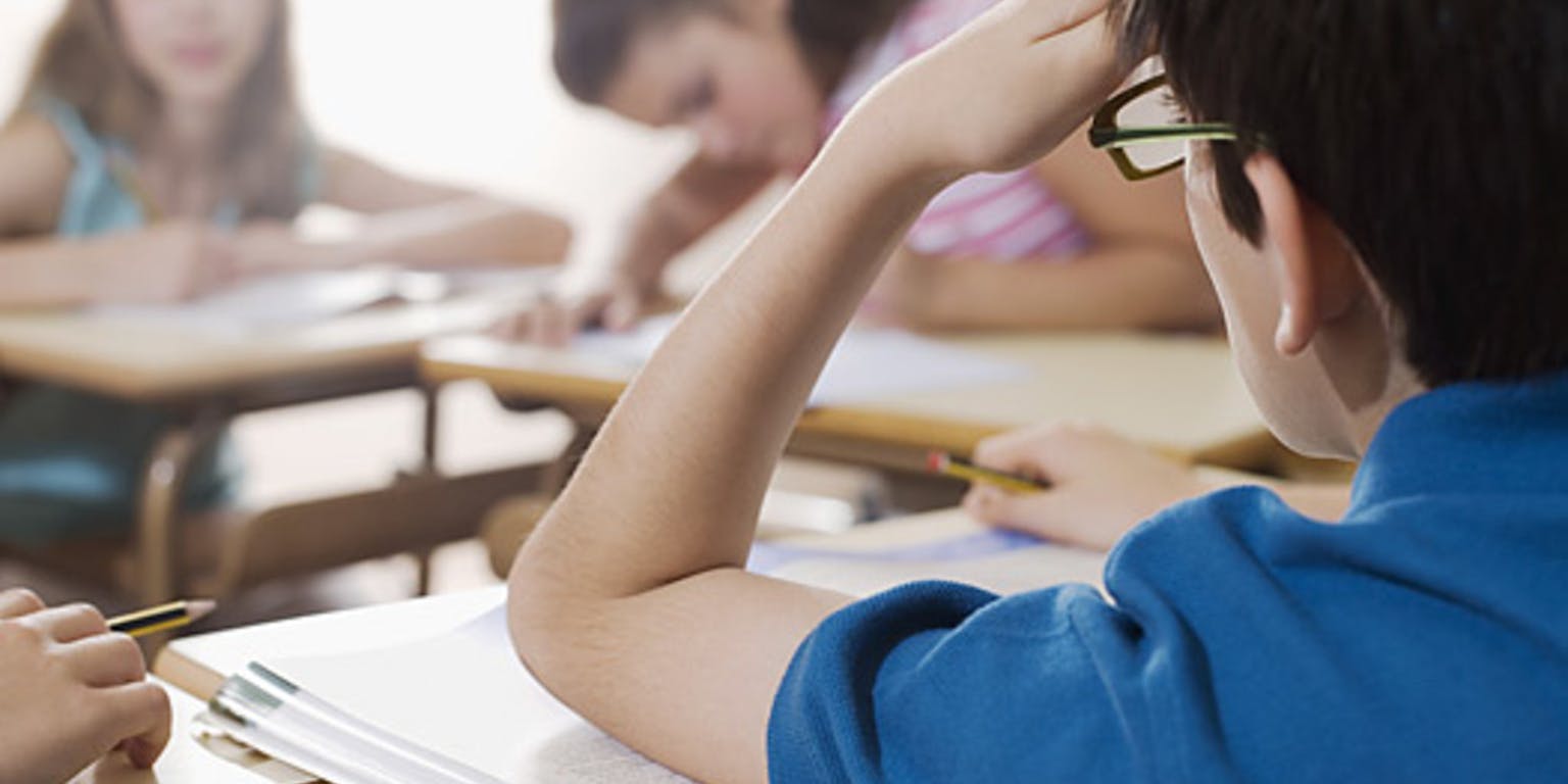 In een klaslokaal zit een jongen aan een bureau.