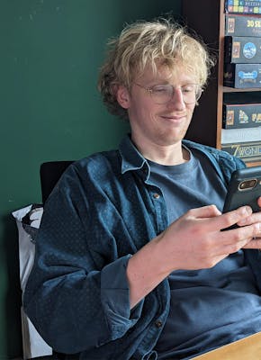 Kas Jansma bekijkt, zittend aan zijn bureau, glimlachend een meme op de smartphone in zijn handen.