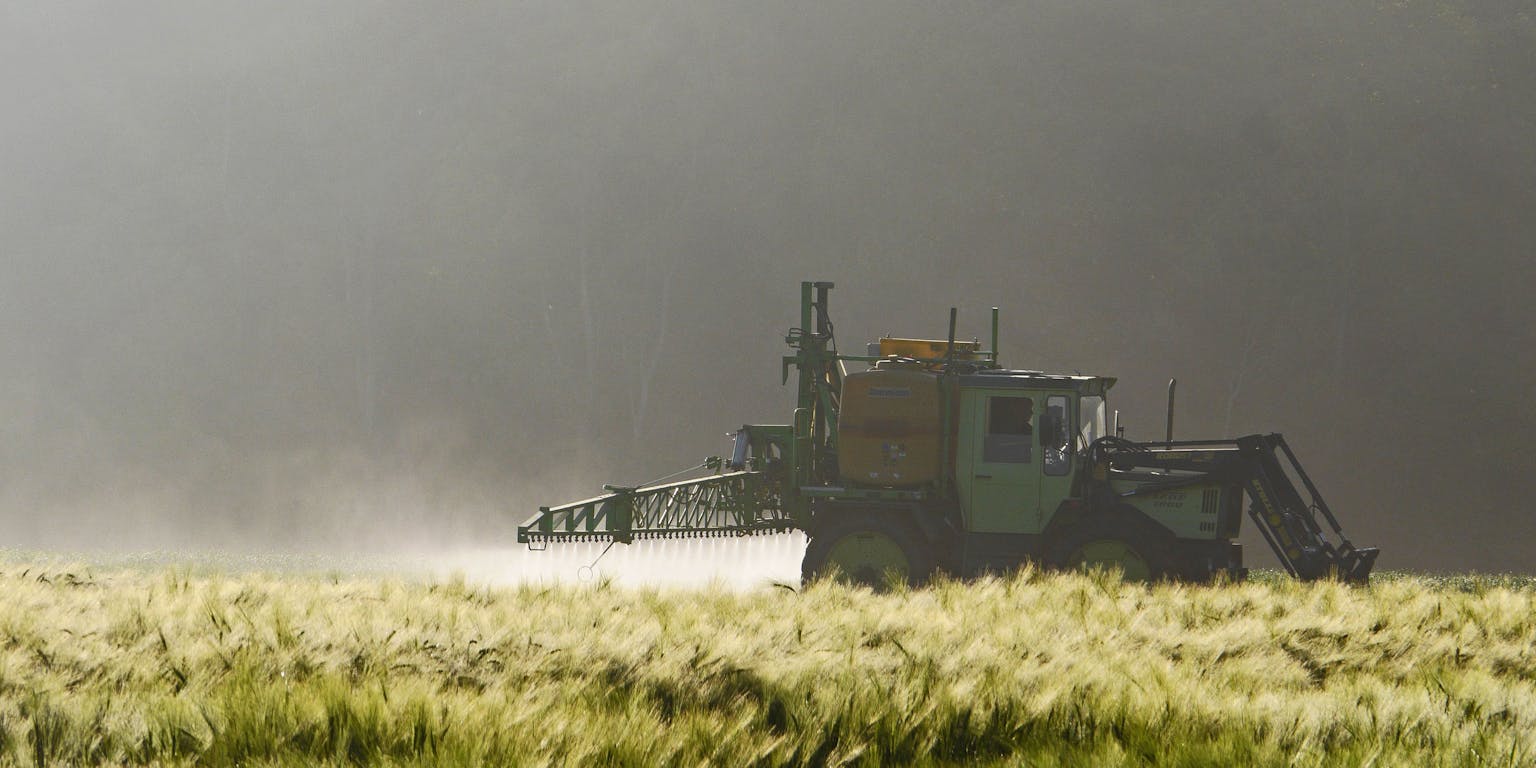 Een landbouwvoertuig besproeit een veld met pesticide.