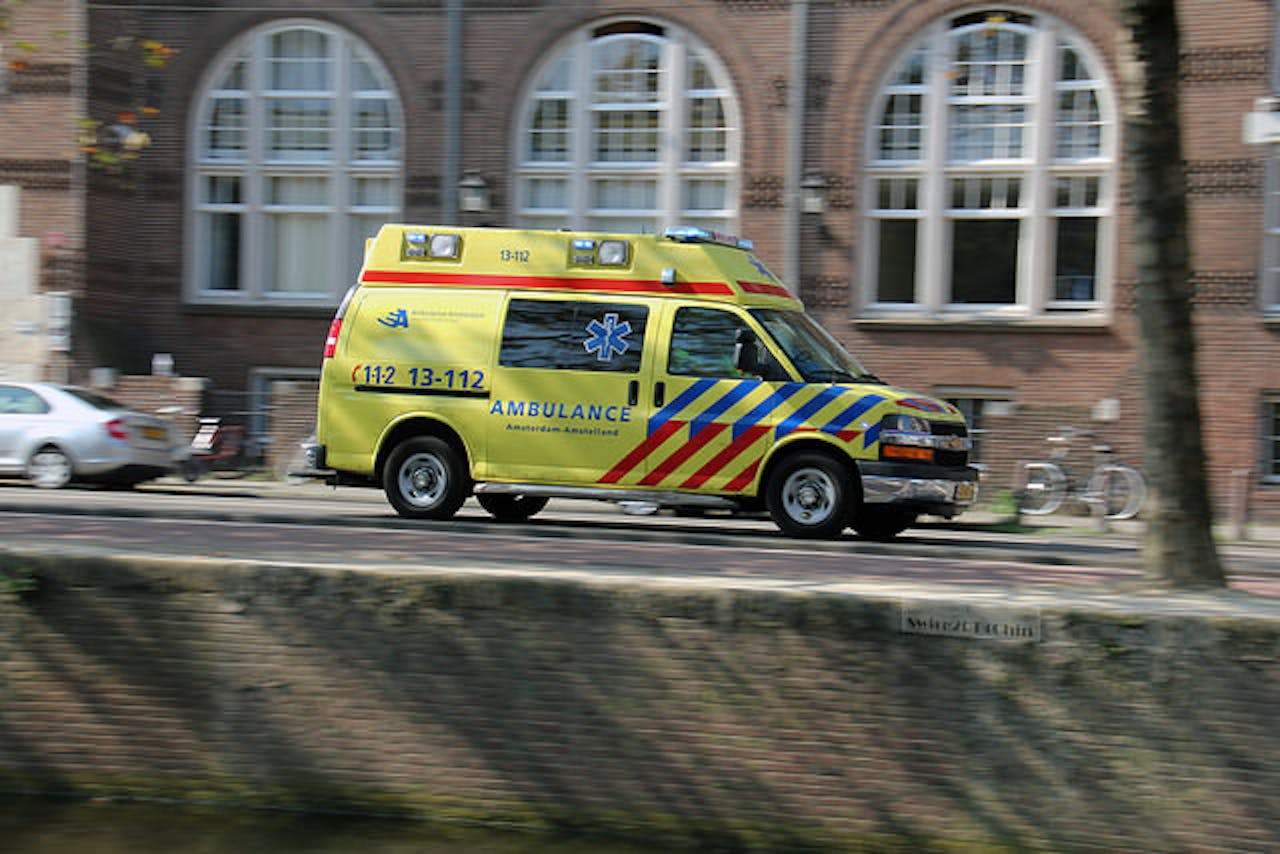 Een gele ambulance rijdt door de straat.