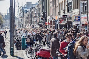 Een menigte mensen die door een straat in Amsterdam loopt.