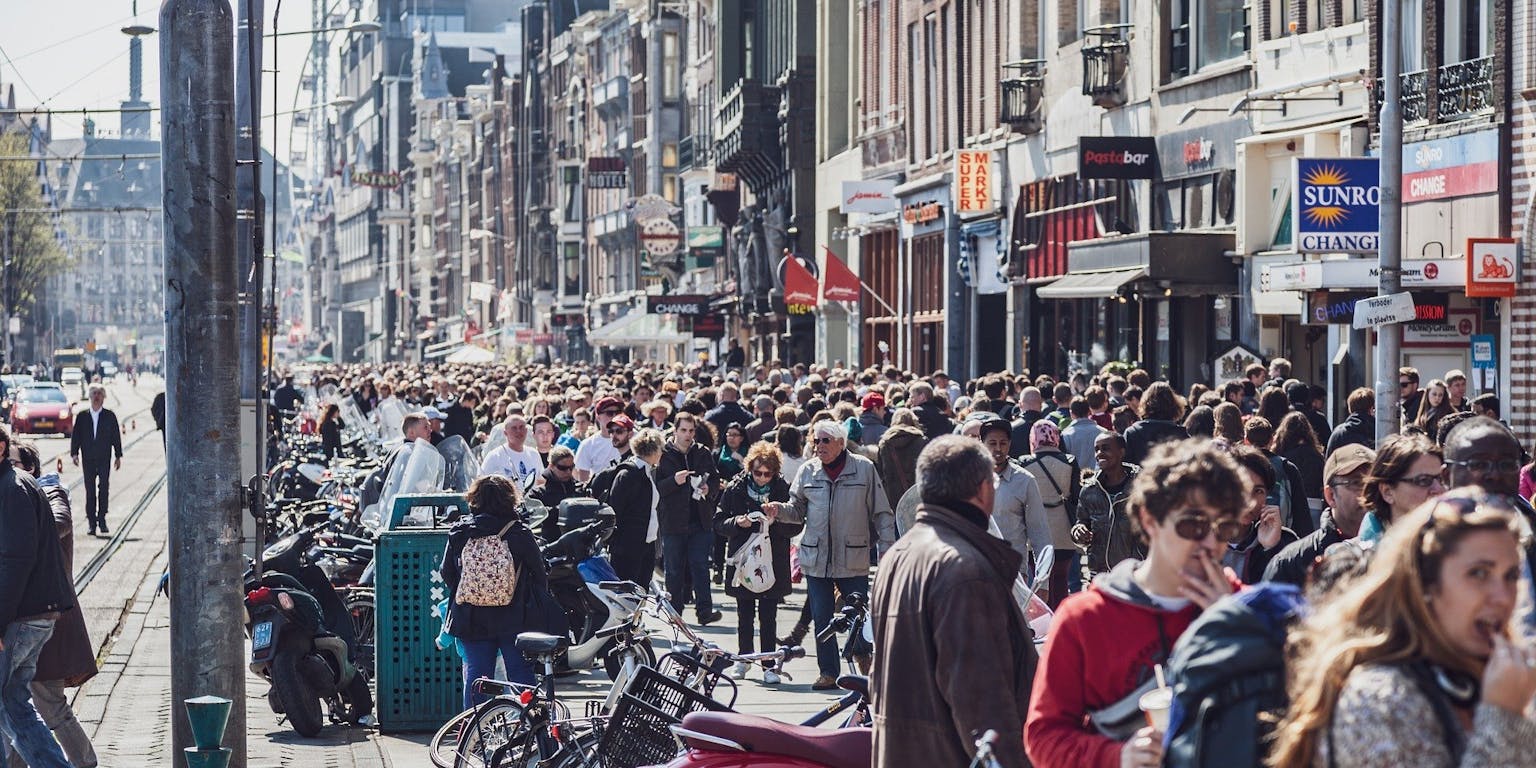 Een menigte mensen die door een straat in Amsterdam loopt.