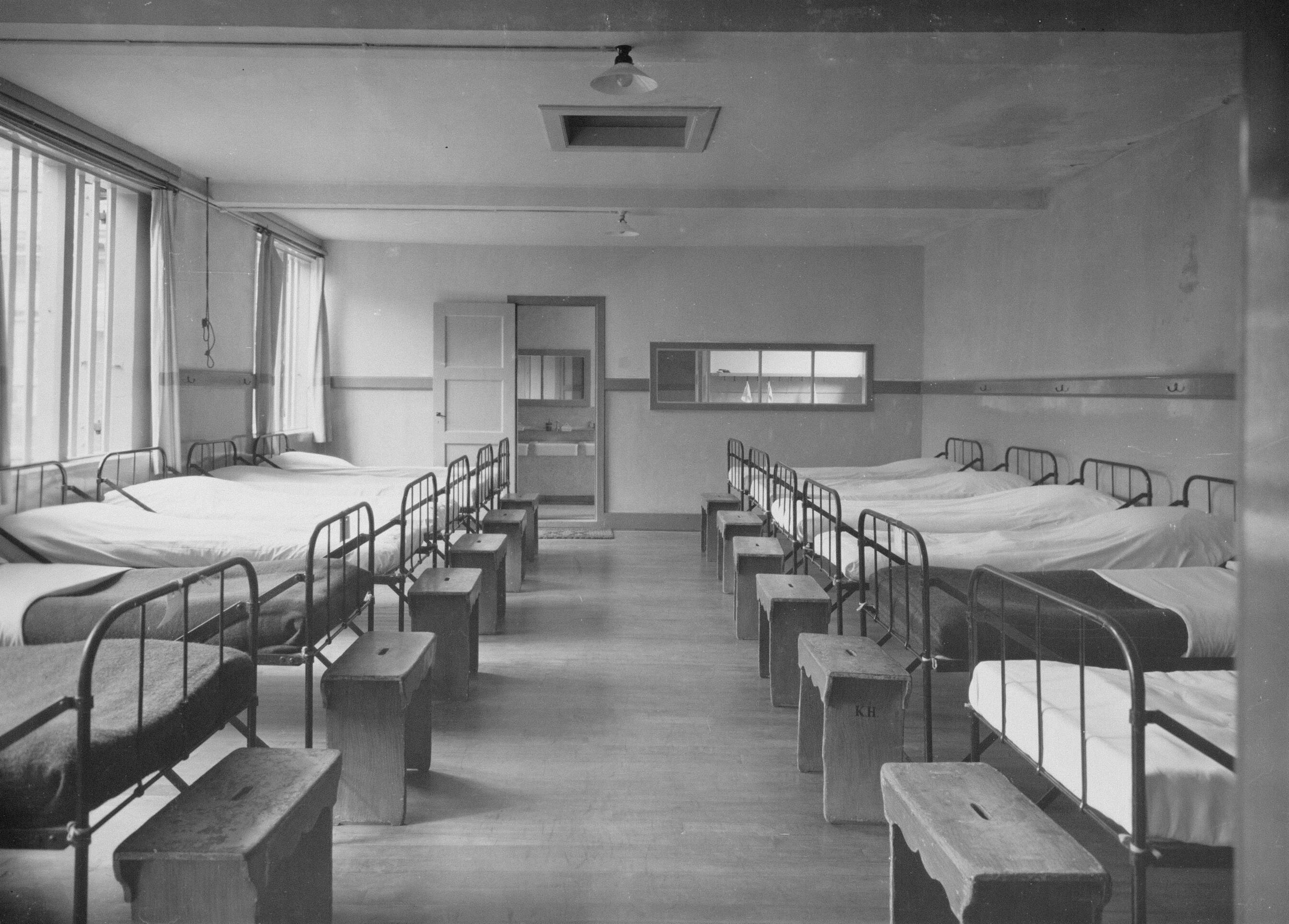 Zwart-witfoto van 10 bedden op een slaapzaal.