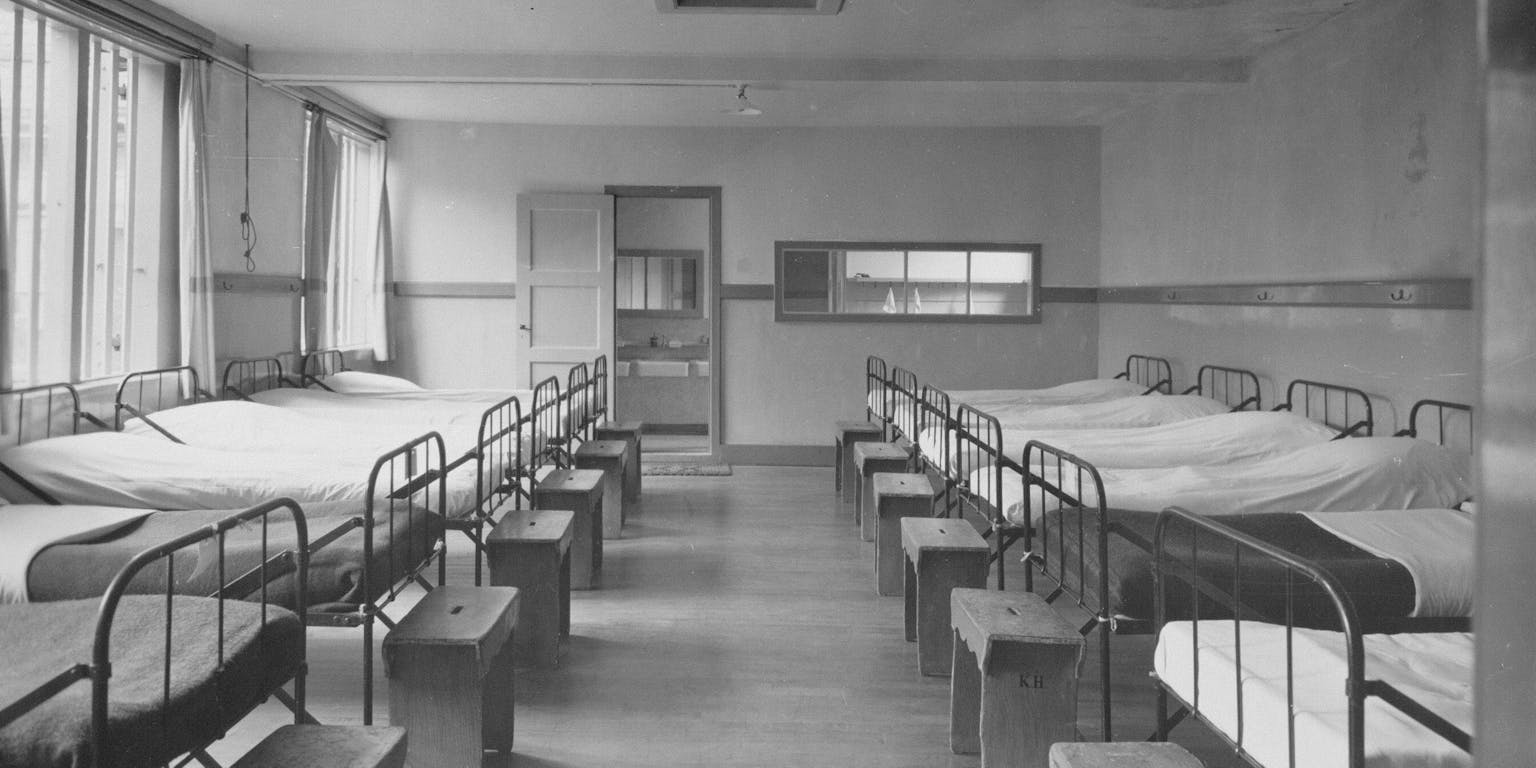 Zwart-witfoto van 10 bedden op een slaapzaal.