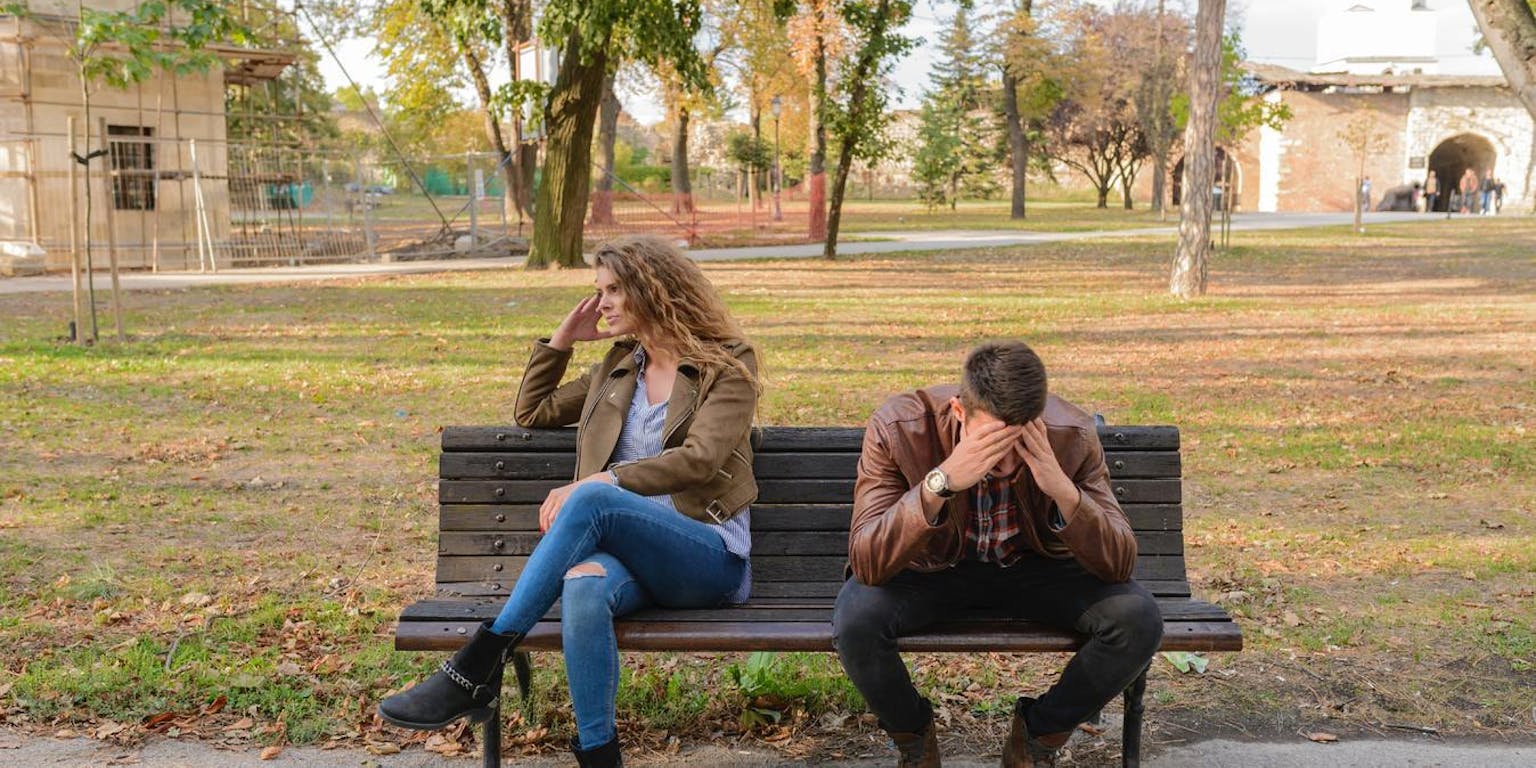 Een man en een vrouw op een bankje in het park. Ze zitten ver uit elkaar en hebben ruzie gehad.