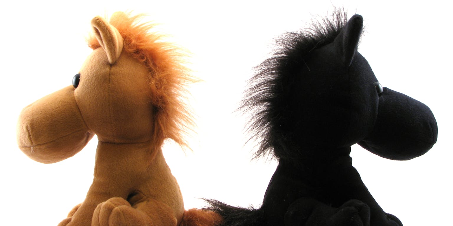 Een zwart en bruin knuffelpaard die met de ruggen naar elkaar toe zitten.