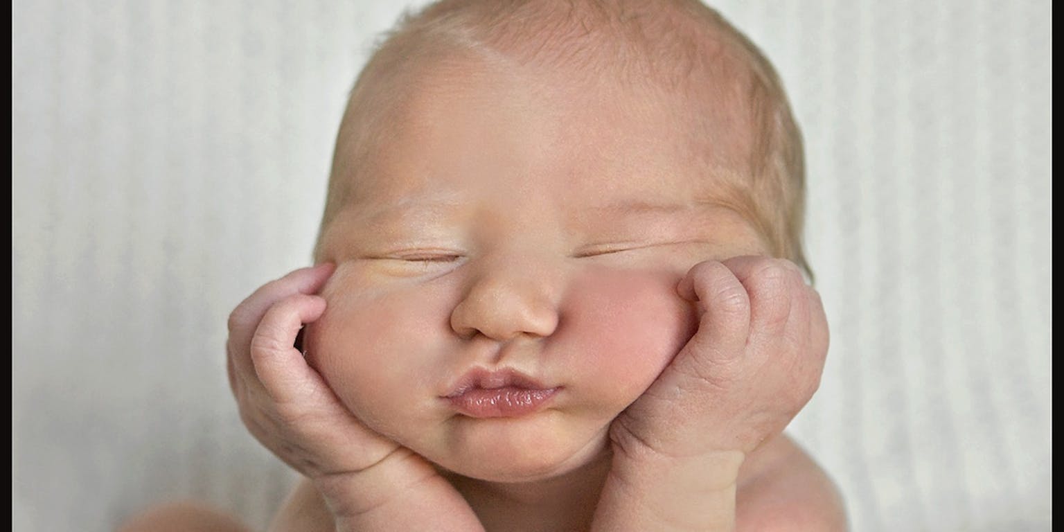 Een baby ligt op een vloer vol roze bloemblaadjes.