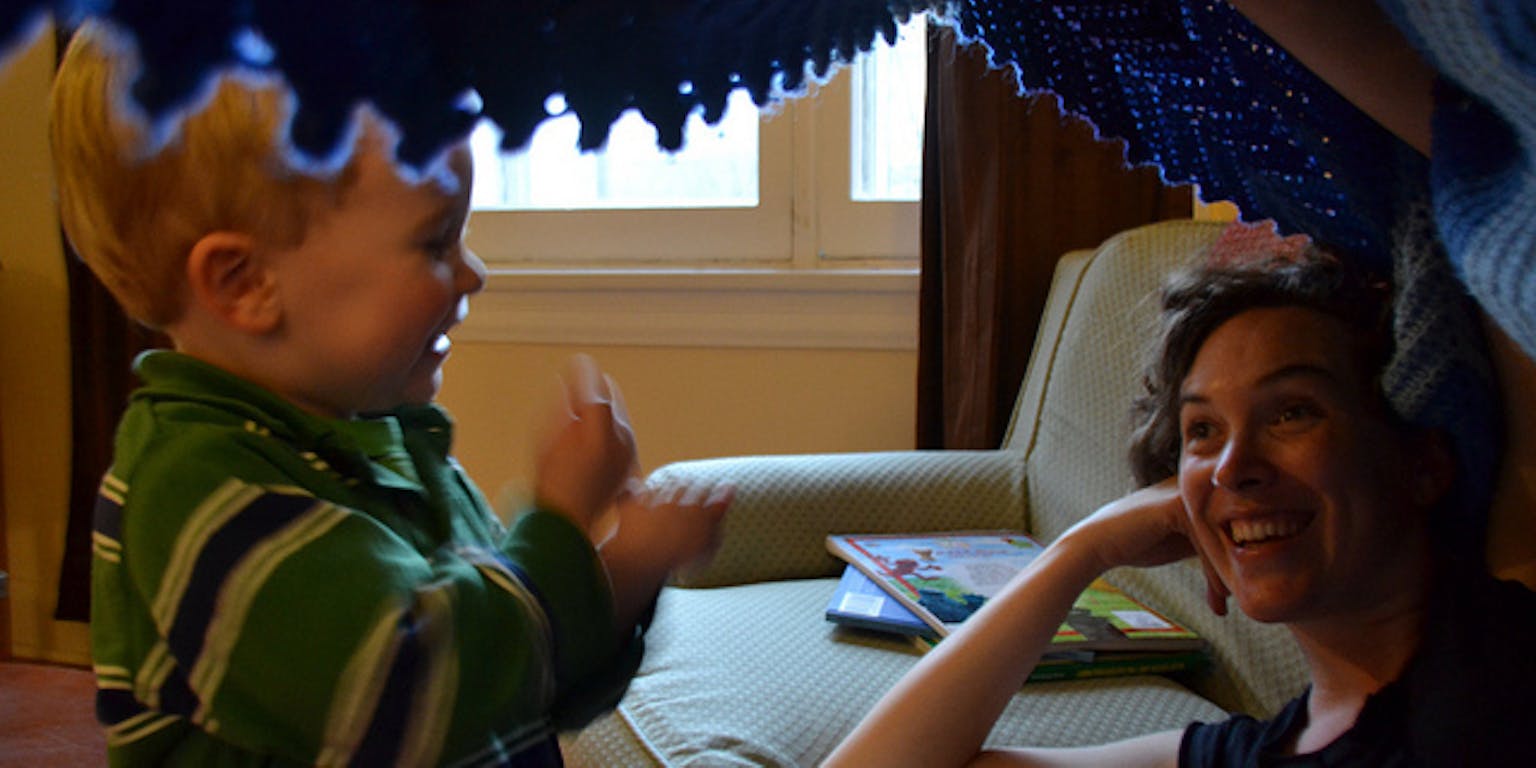 Een vrouw en een kind onder een blauwe deken bij de bank.