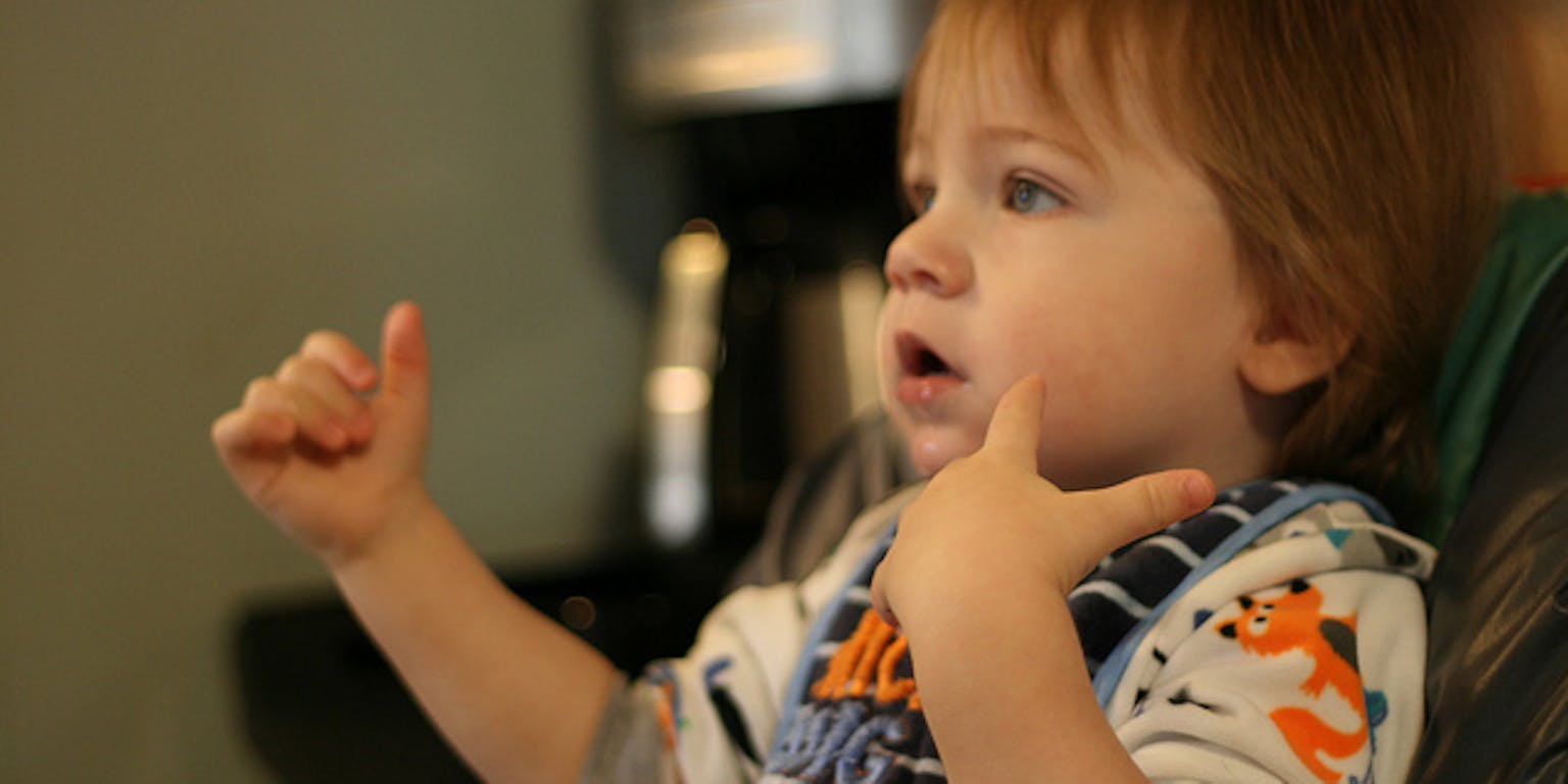 Een baby in een stoel die gebaren maakt met de handen.