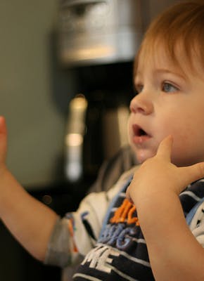 Een baby in een stoel die gebaren maakt met de handen.