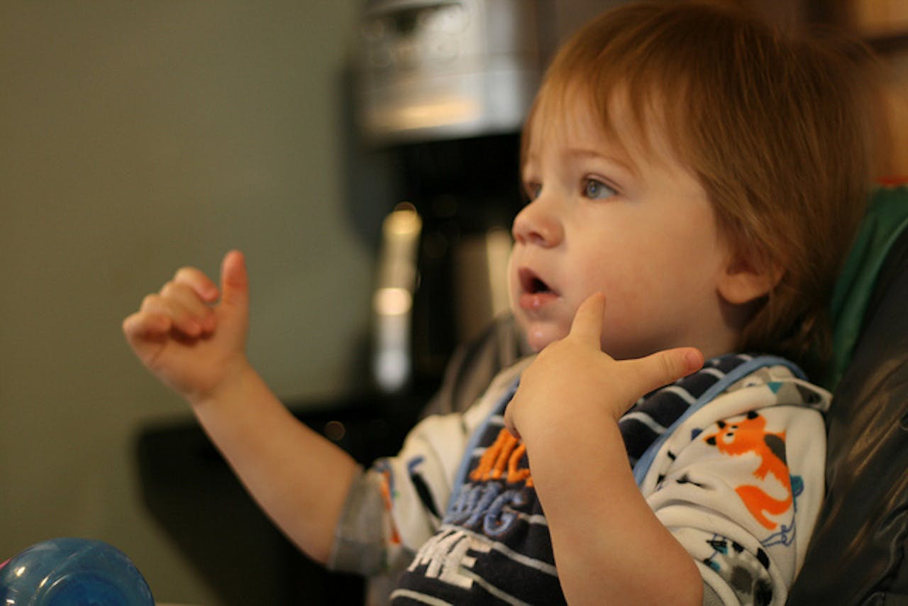 Een baby in een stoel die gebaren maakt met de handen.
