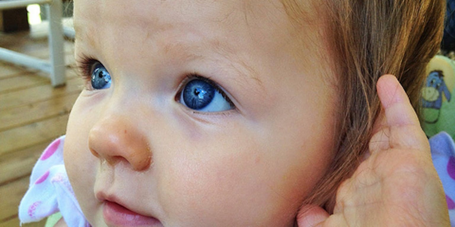 Een close up van een babygezicht met fel blauwe ogen.