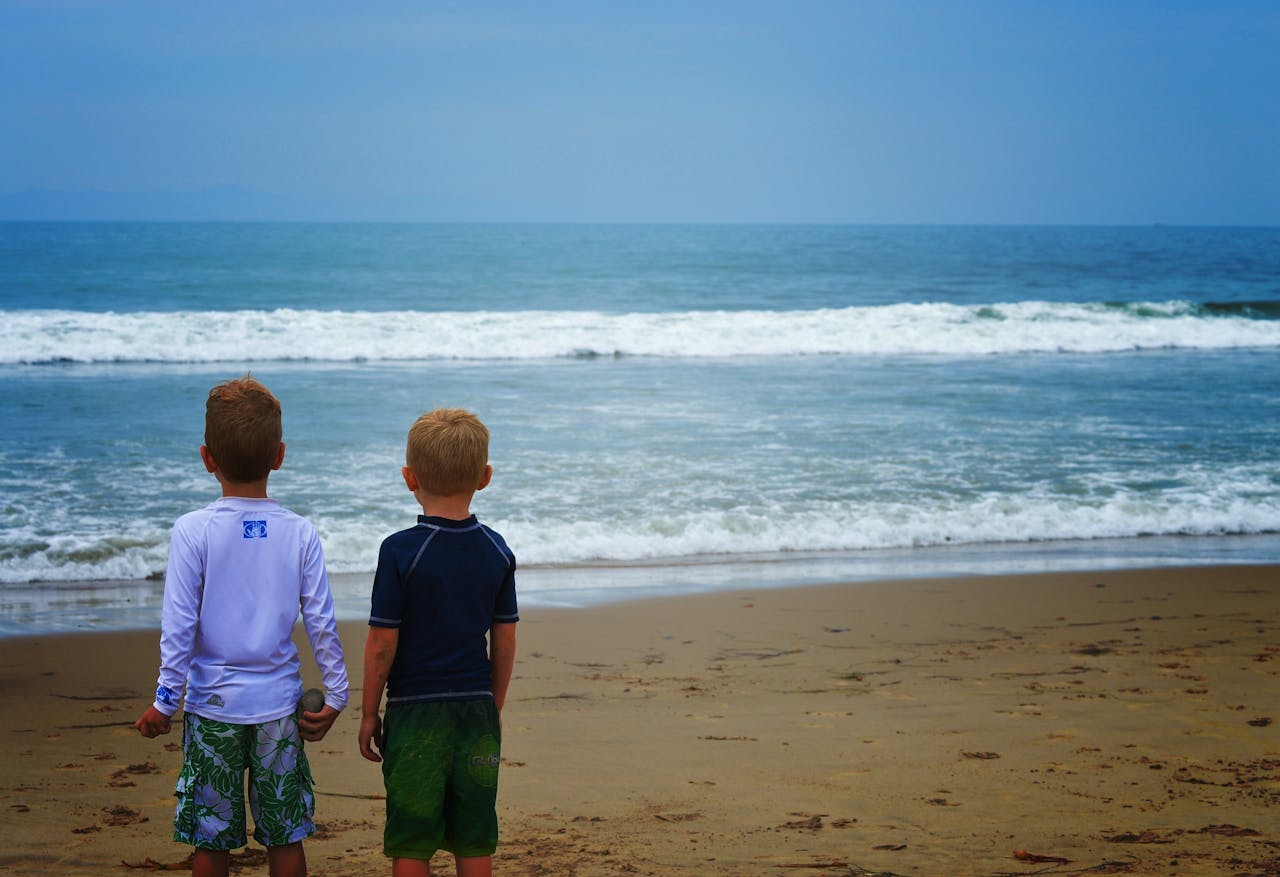 Twee kinderen staan op het strand en kijken naar de zee.