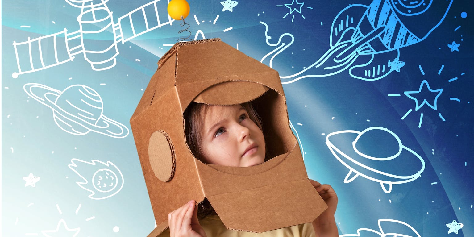 Een meisje heeft een van karton gemaakte ruimtehelm op. Op de blauwe achtergrond zijn met wit planeten, raketten en satellieten getekend.