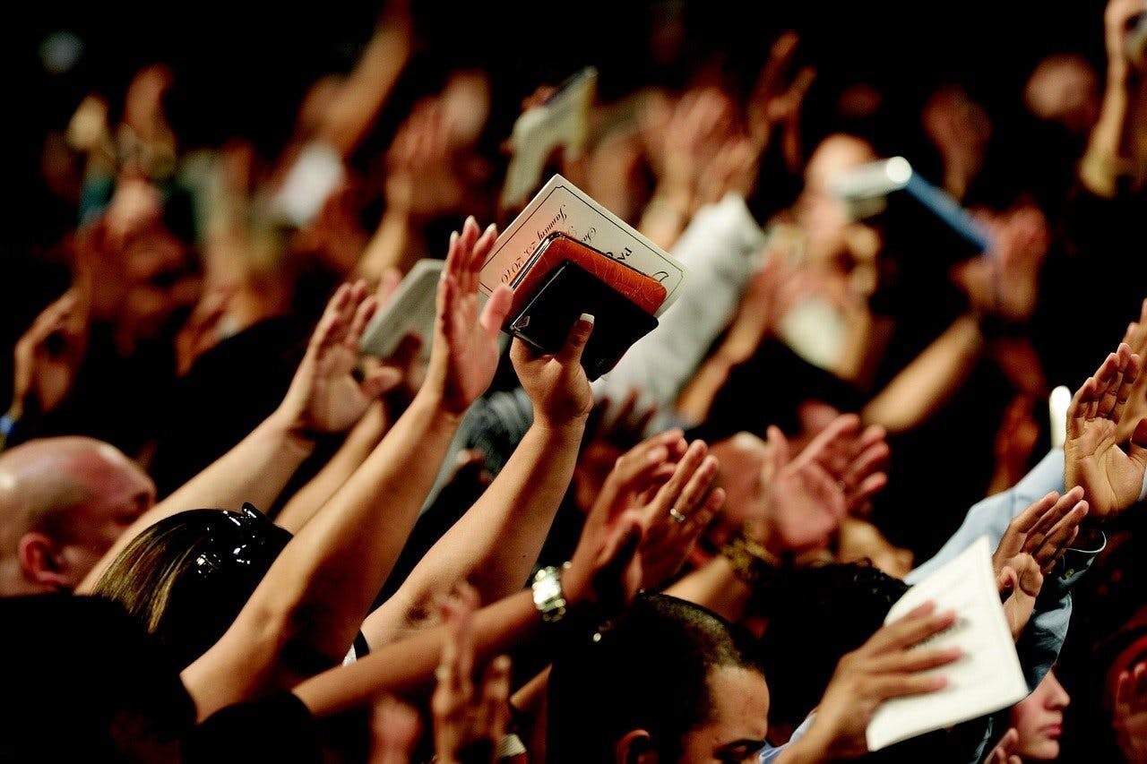 Een menigte mensen met hun handen in de lucht. Ze zijn aan het bidden.