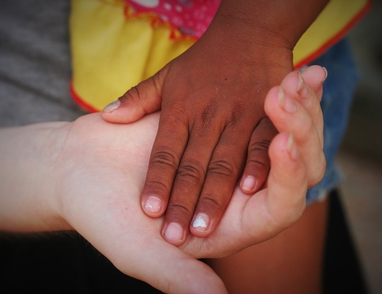 De hand van een persoon ligt in de hand van een tweede persoon. De handen hebben allebei een andere huidskleur.