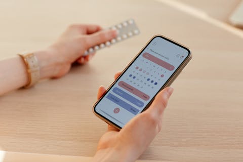 Veel vrouwen tracken hun menstruatiecyclus met behulp van een app op hun telefoon smartphone met app op je menstruatiecyclus bij te houden, en in een andere hand een strip met de anticonceptiepil