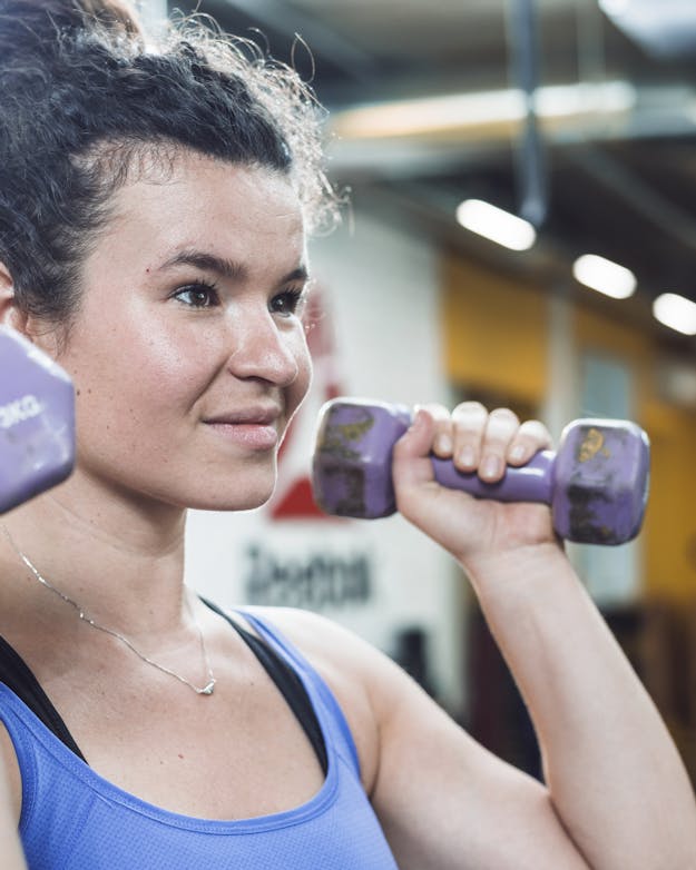 Niet je hormonale fase, maar je gevoel moet leidend zijn in je training Witte vrouw met donker haar in een knot die in de sportschool gewichten tilt