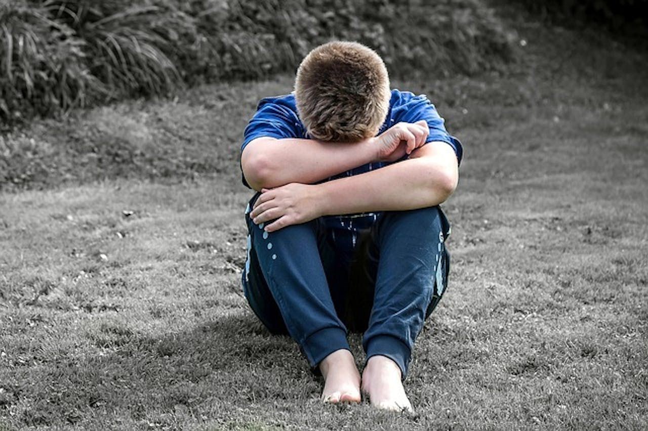 Een jongen zit in het gras met zijn handen op zijn knieën.