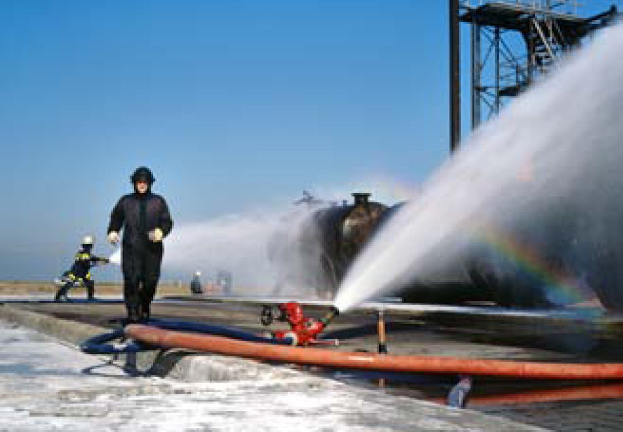 Een brandweerman spuit water uit een brandkraan.