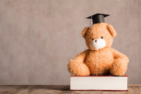 Een teddybeer met een afstudeerpet zit op een boek.