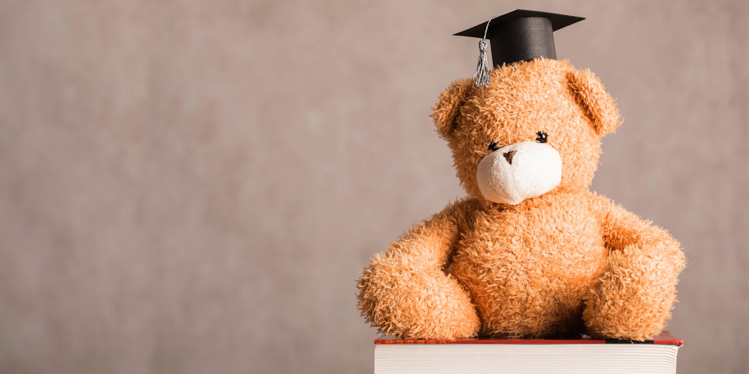 Een teddybeer met een afstudeerpet zit op een boek.