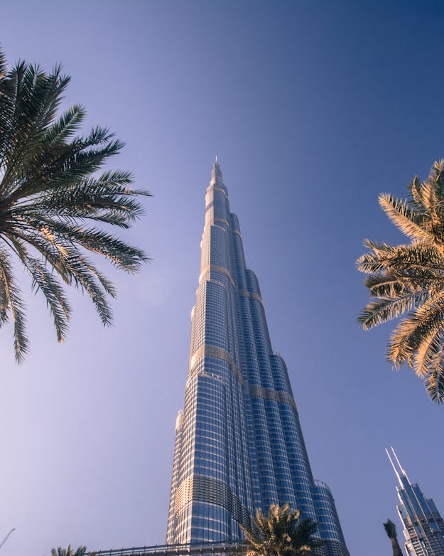 Twee palmbomen met daartussen een wolkenkrabber van staal en glas van onder af bekeken tegen een blauwe lucht. Twee palmbomen met daartussen een wolkenkrabber van staal en glas van onder af bekeken tegen een blauwe lucht.