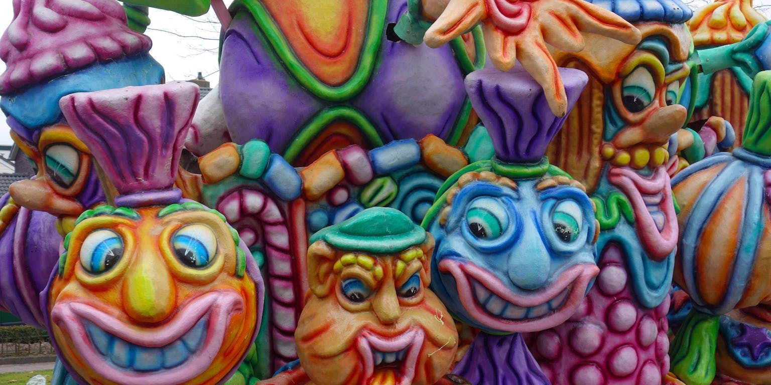 Een close-up van een kleurrijke praalwagen tijdens carnaval. Er zijn vijf grappige gezichten te zien.