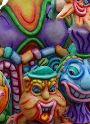 Een close-up van een kleurrijke praalwagen tijdens carnaval. Er zijn vijf grappige gezichten te zien.