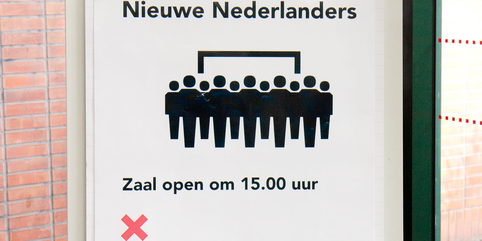 Een bord op een gebouw met de tekst: ceremonie nieuwe Nederlanders. Zaal open om 15:00 uur. De drie rode kruizen van Amsterdam zijn ook te zien. Ook zien we een groep met poppetjes.