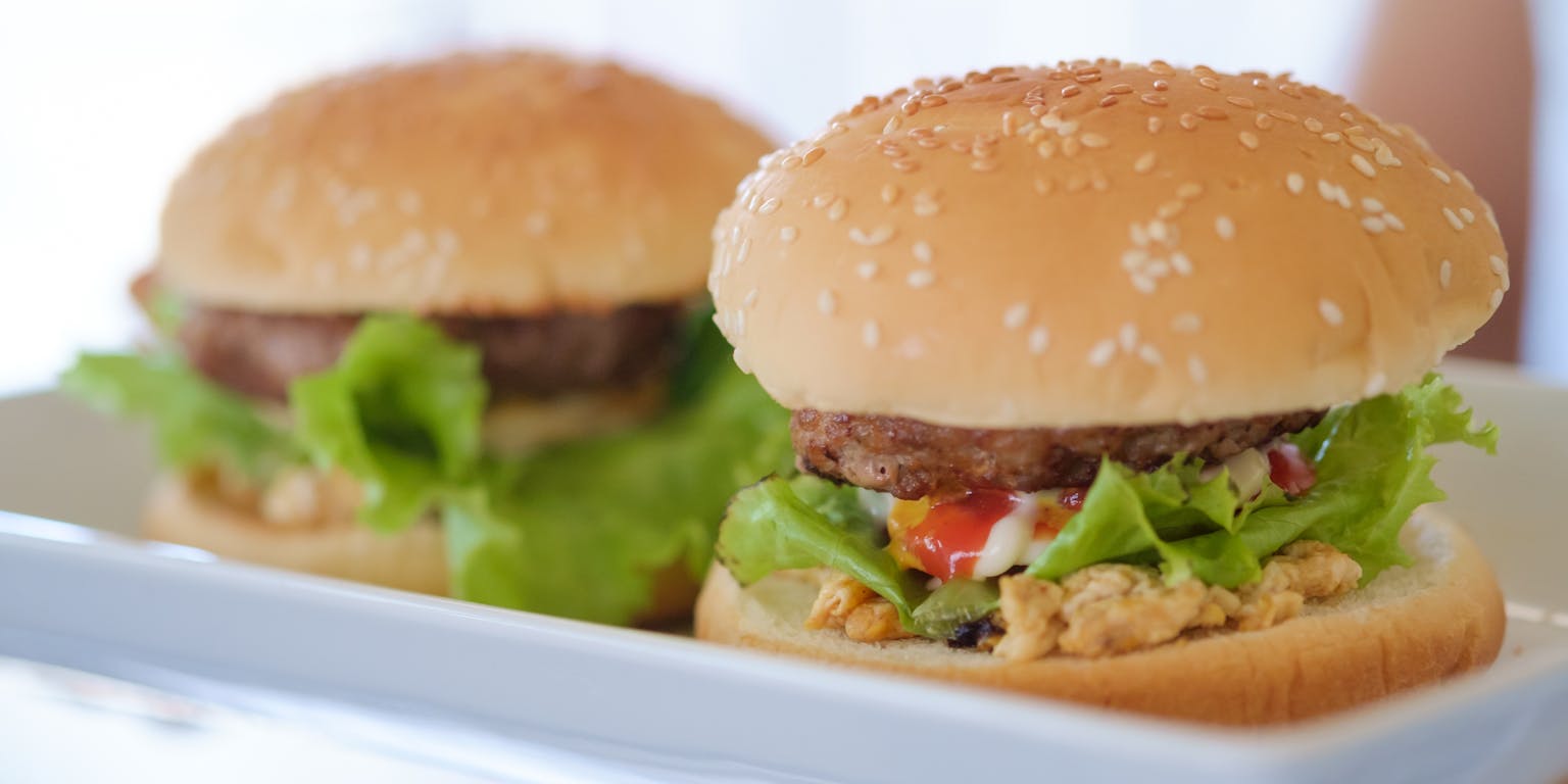 Een wit rechthoekig bord met daarop twee broodjes hamburger.
